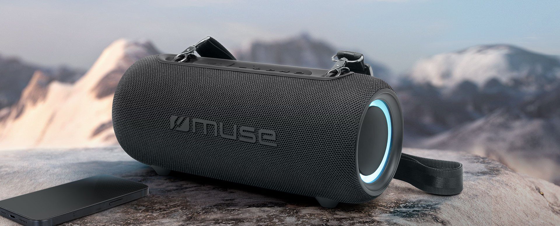 A MUSE portable Bluetooth speaker on a rock ledge above a mountain range at dusk