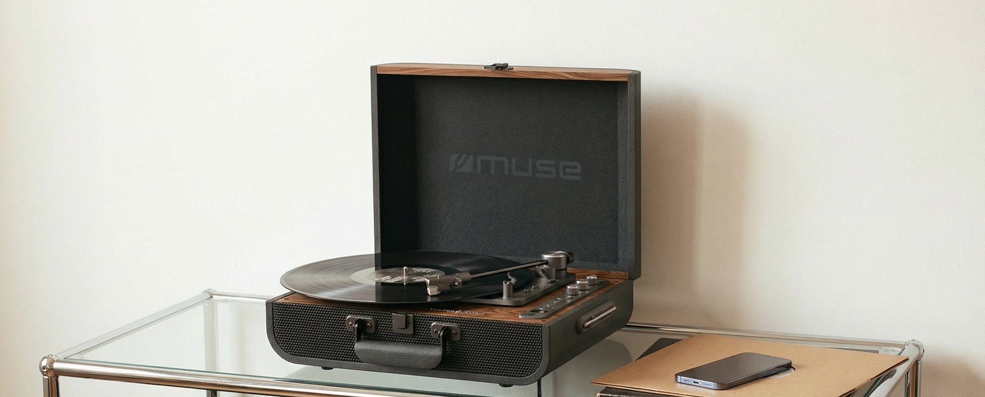A MUSE suitcase turntable open on a glass table in a sunlit room